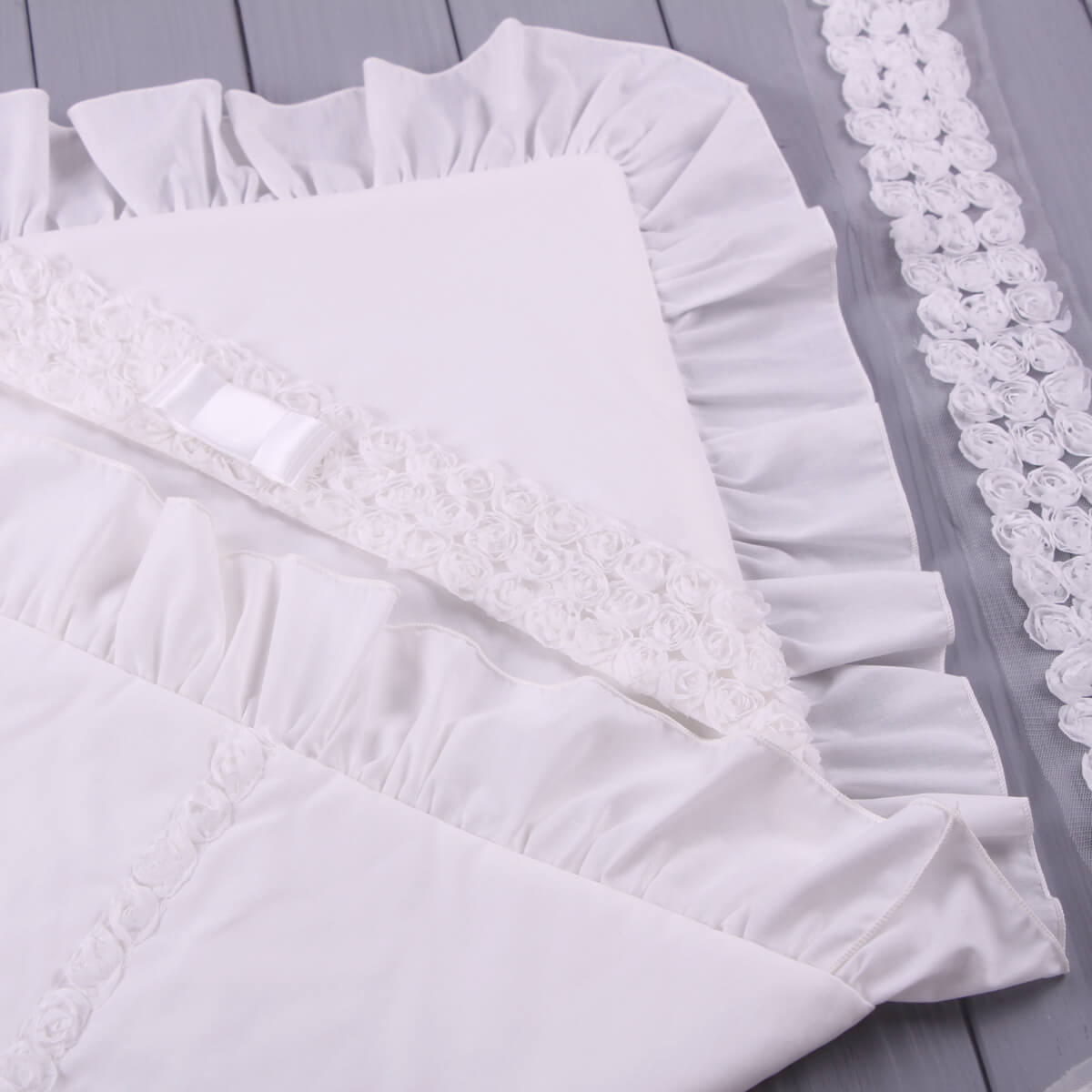 White lace trim christening blanket on a gray wooden surface