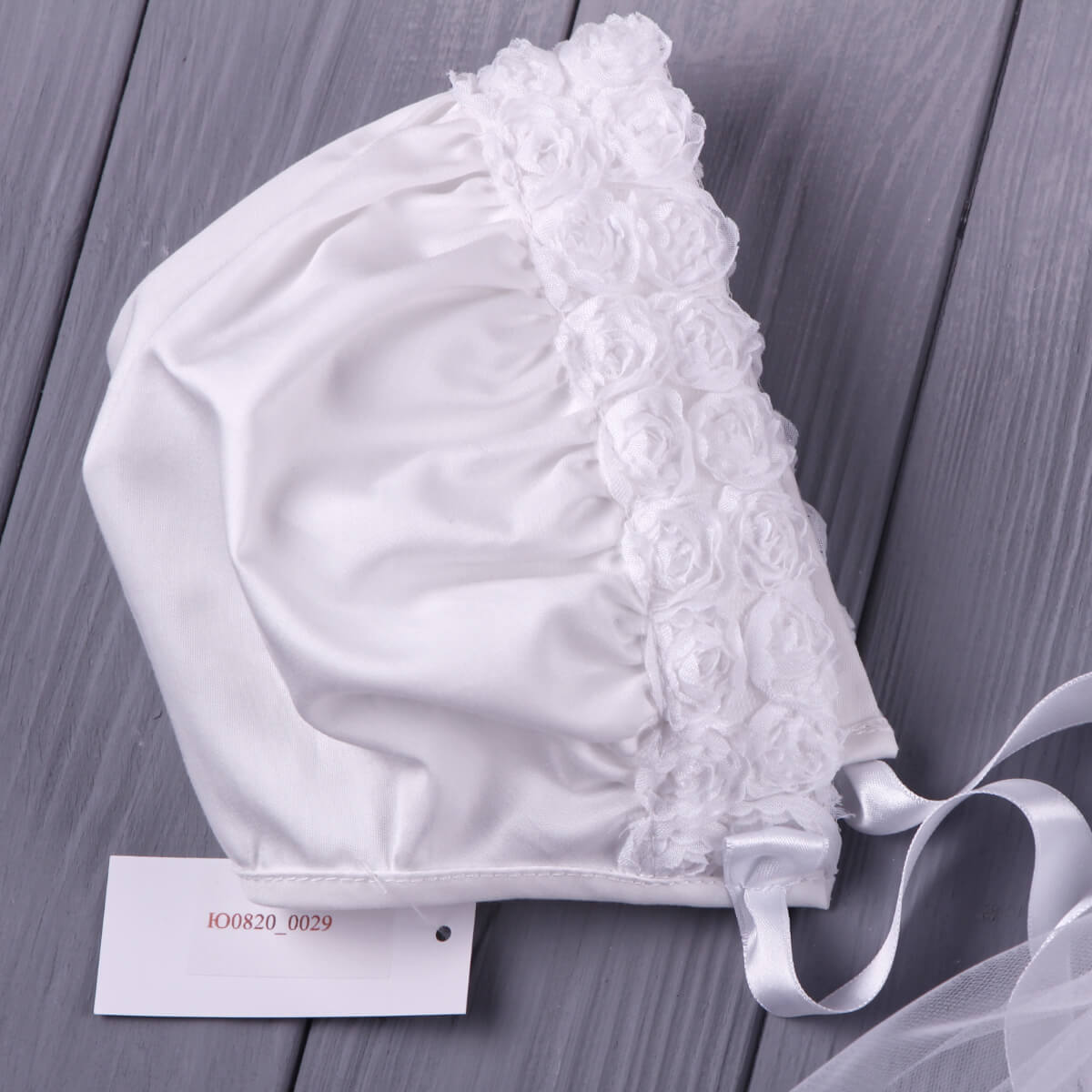 White Vintage Baptism Bonnet on a wooden surface with a label.