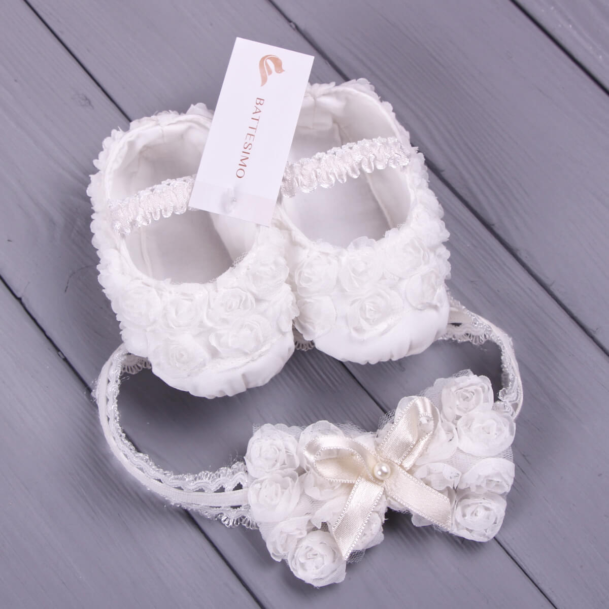 Christening Booties and headband set on a wooden surface with a visible brand tag.