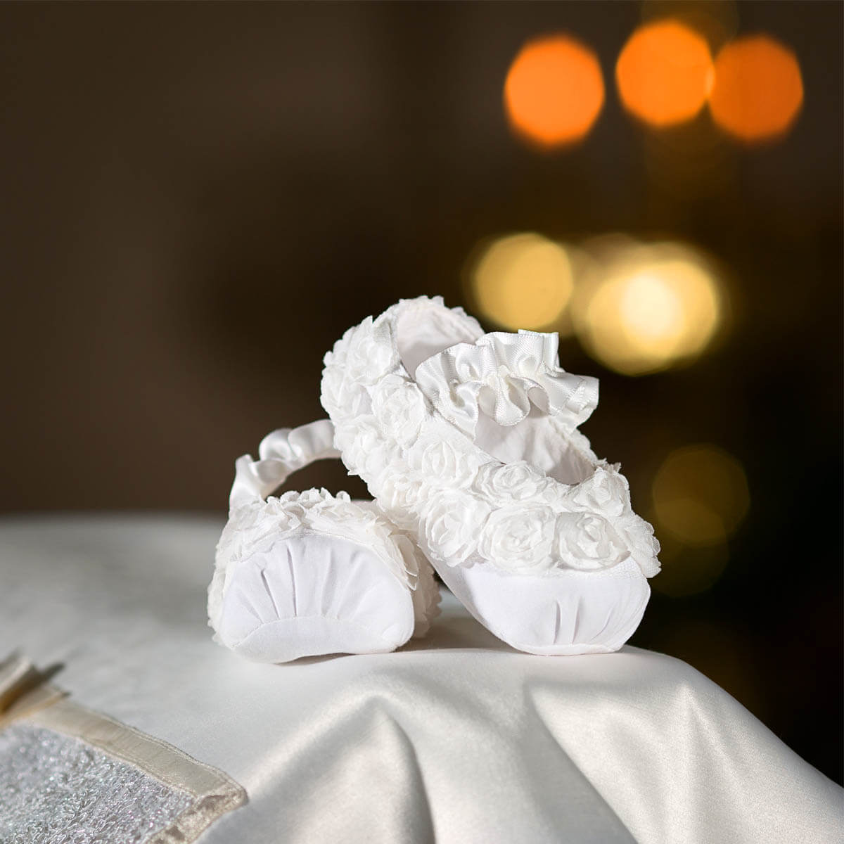 Pair of Christening Booties on a textured surface with blurred lights in the background