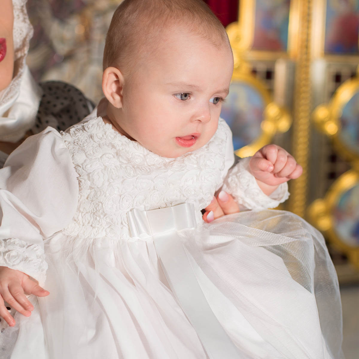 Baby in a Girls Christening Gown with a blurred carousel in the background