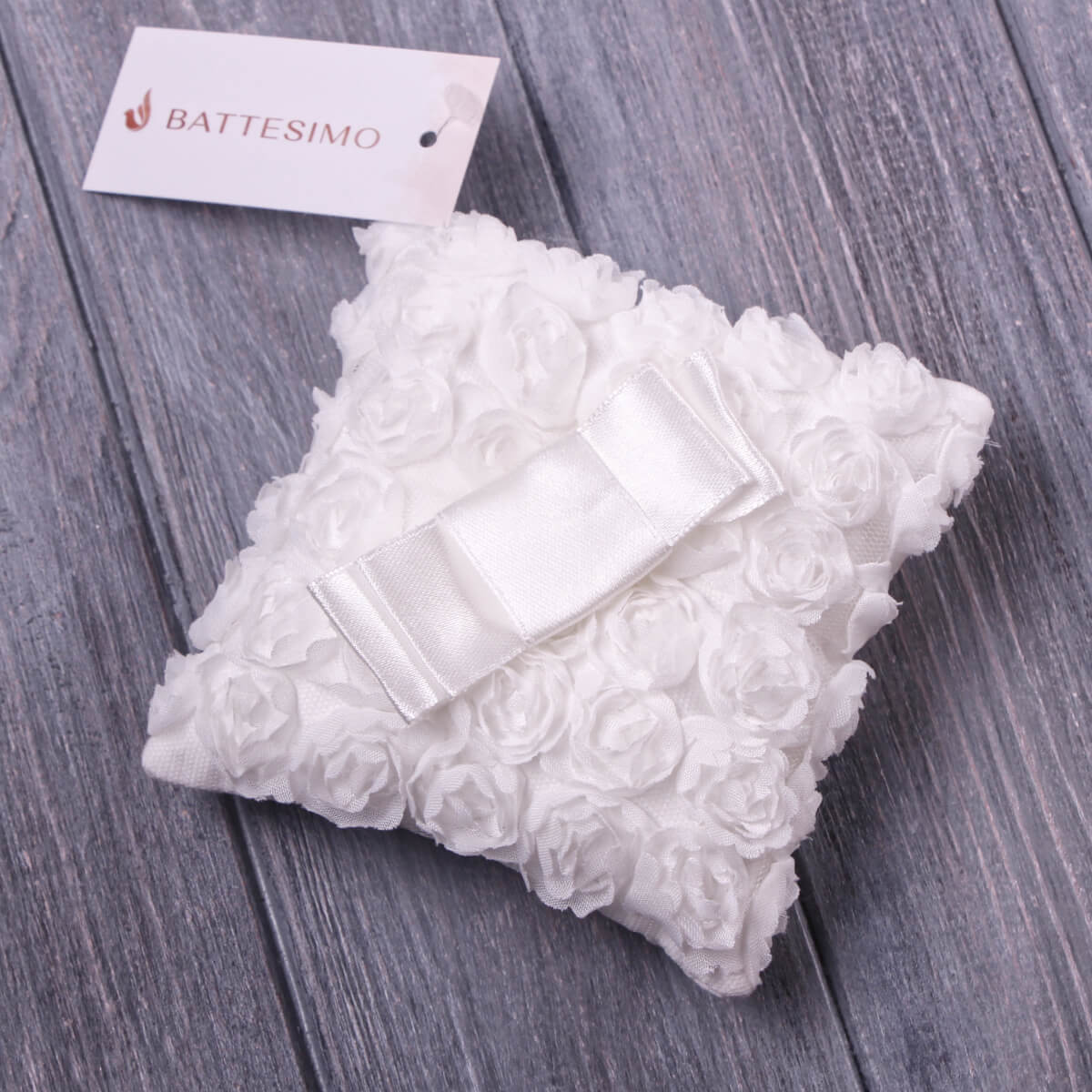 Baptism Ceremony Pillow with a ribbon on a gray wooden surface, featuring a 'Battesimo' tag.