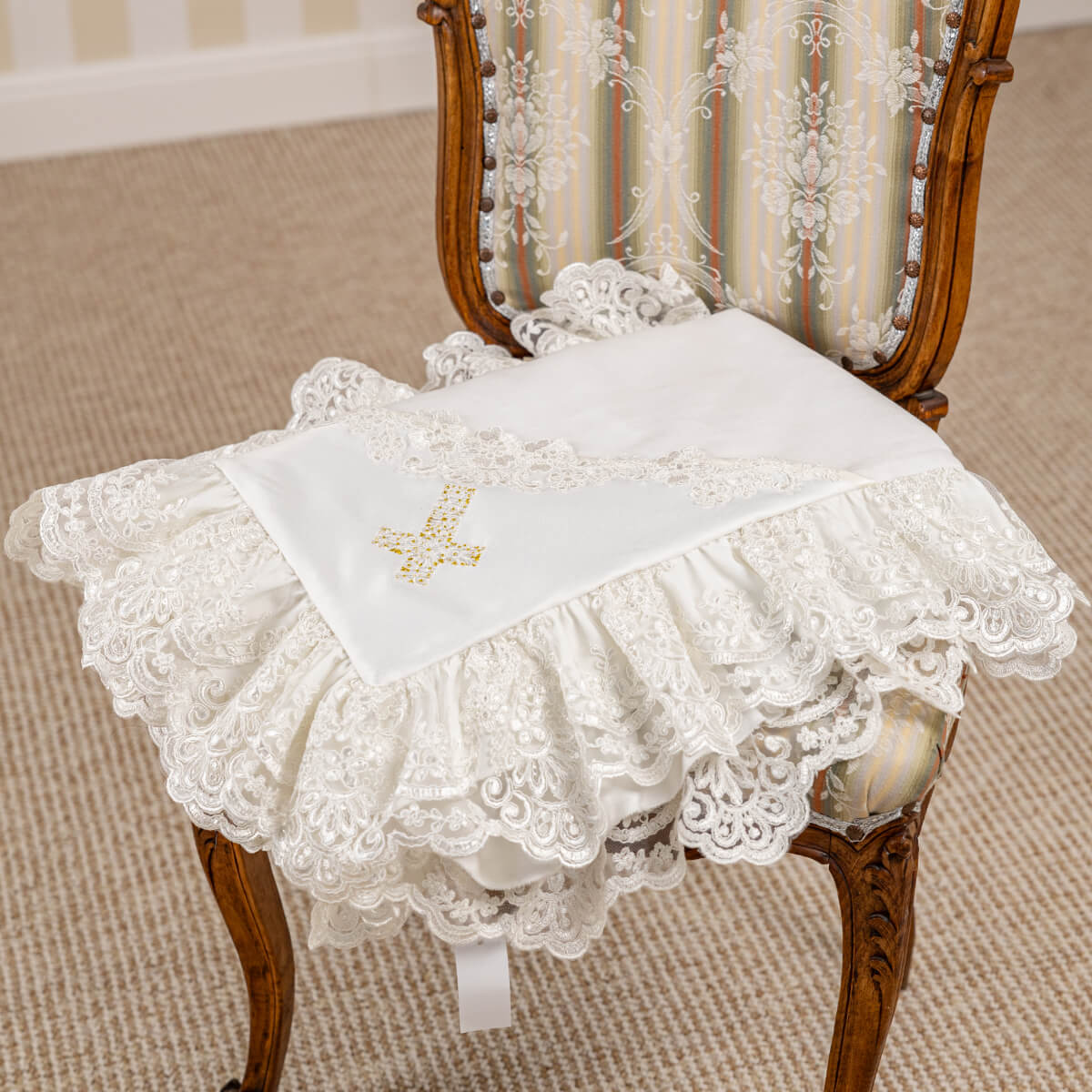 Decorative lace christening blanket on a wooden chair with a white cushion.
