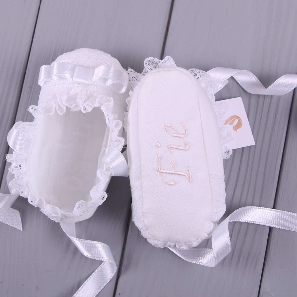Christening Booties with lace details and a ribbon on a gray wooden surface