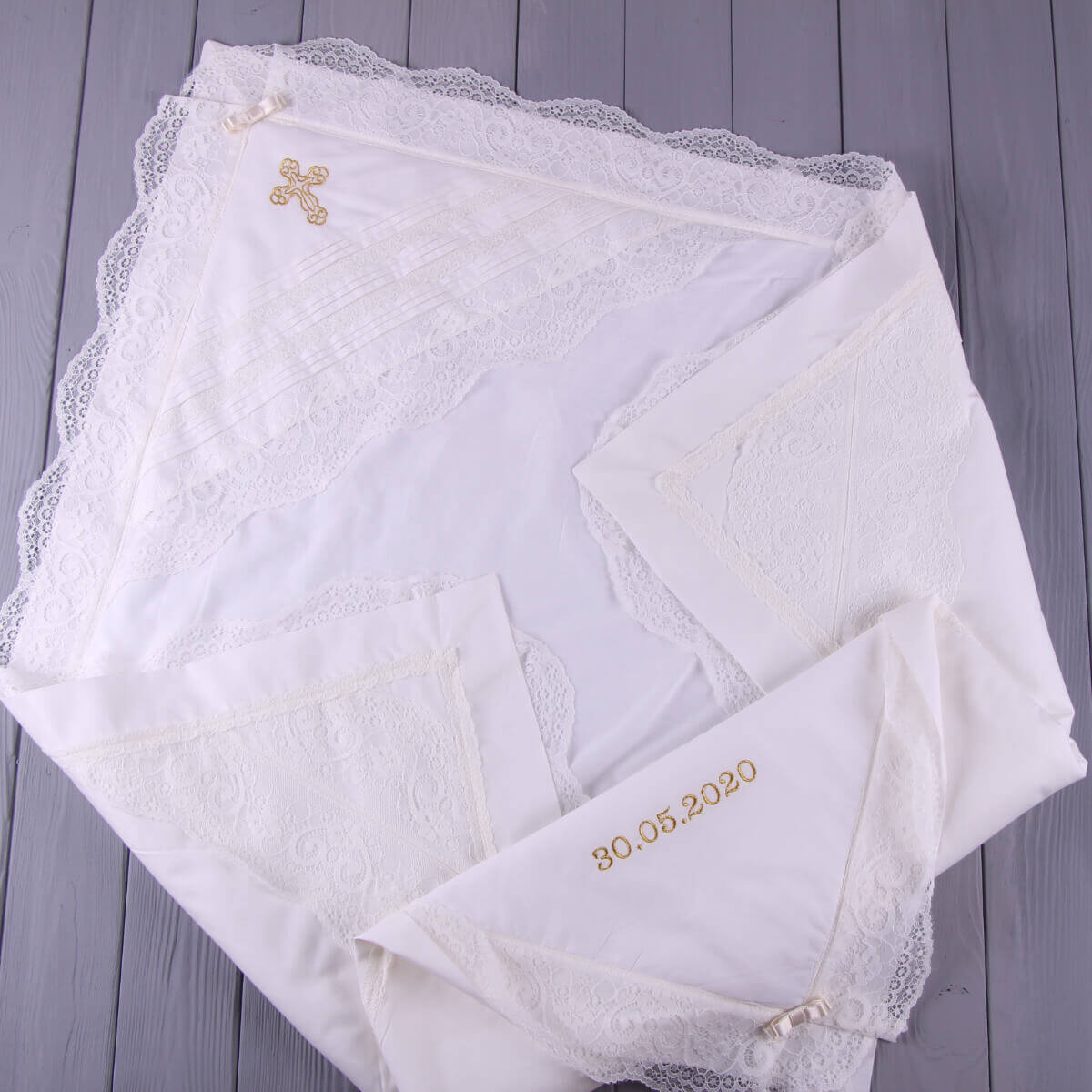 Set of white Christening Blanket with lace edges and embroidered dates on a wooden surface
