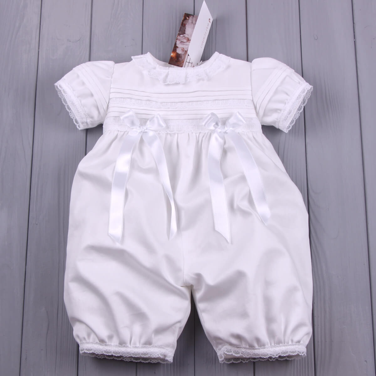 Christening romper with lace details on a gray wooden surface