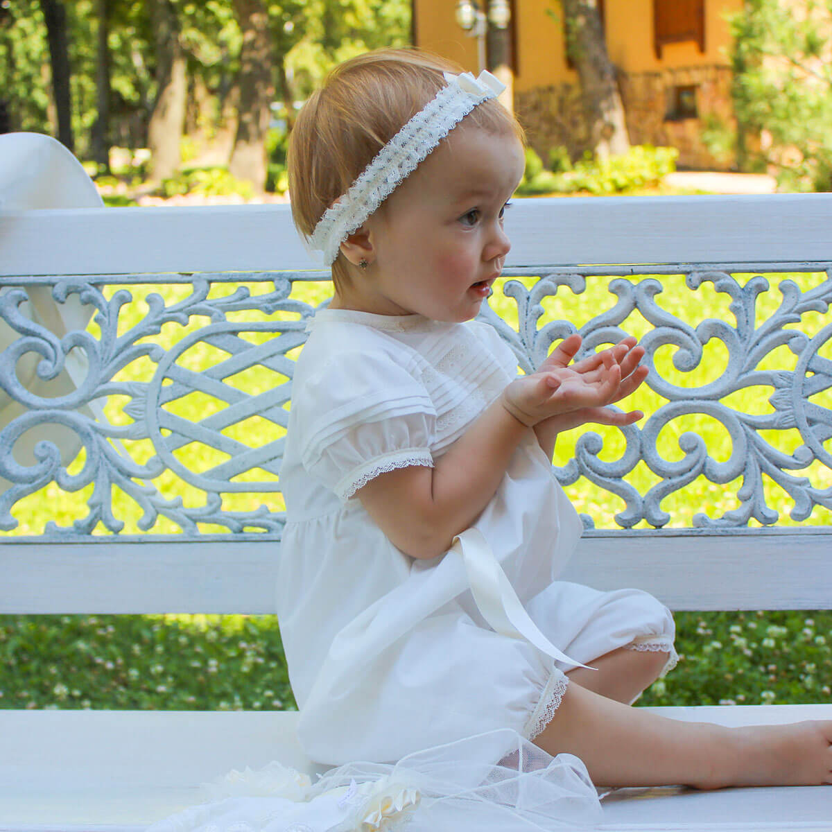 Christening romper sitting on a decorative bench outdoors.