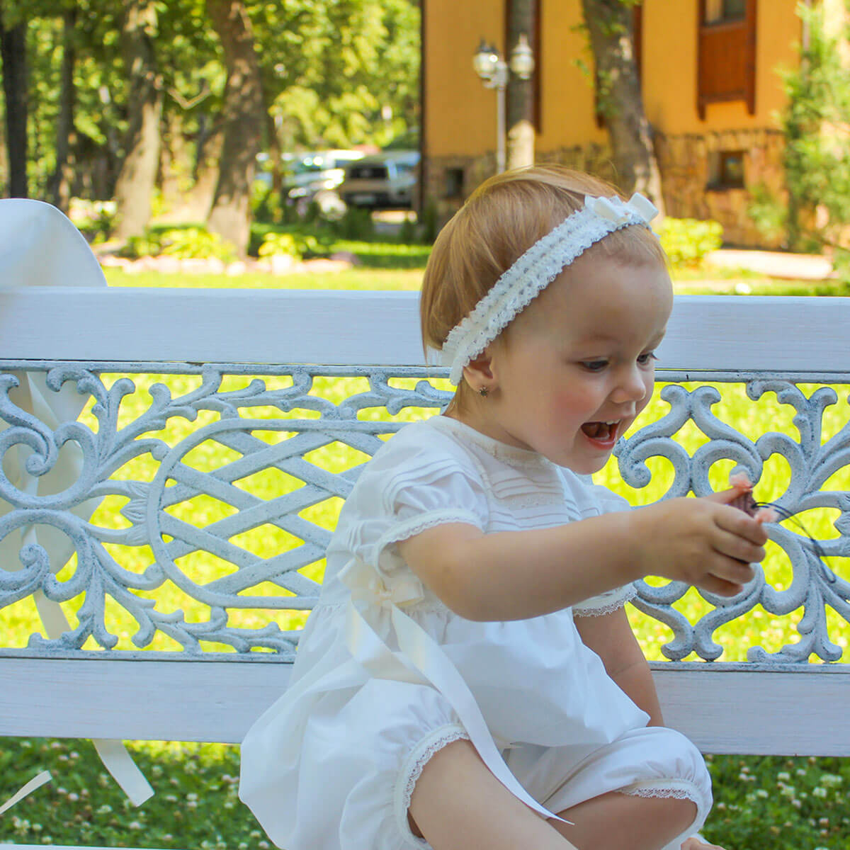 Christening romper sitting on a decorative bench outdoors.