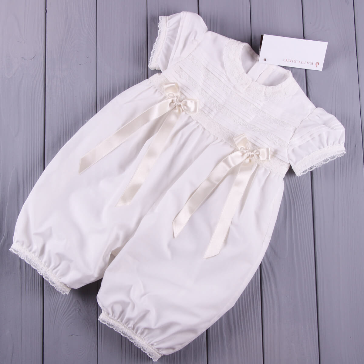 Christening romper with ribbons on a wooden surface