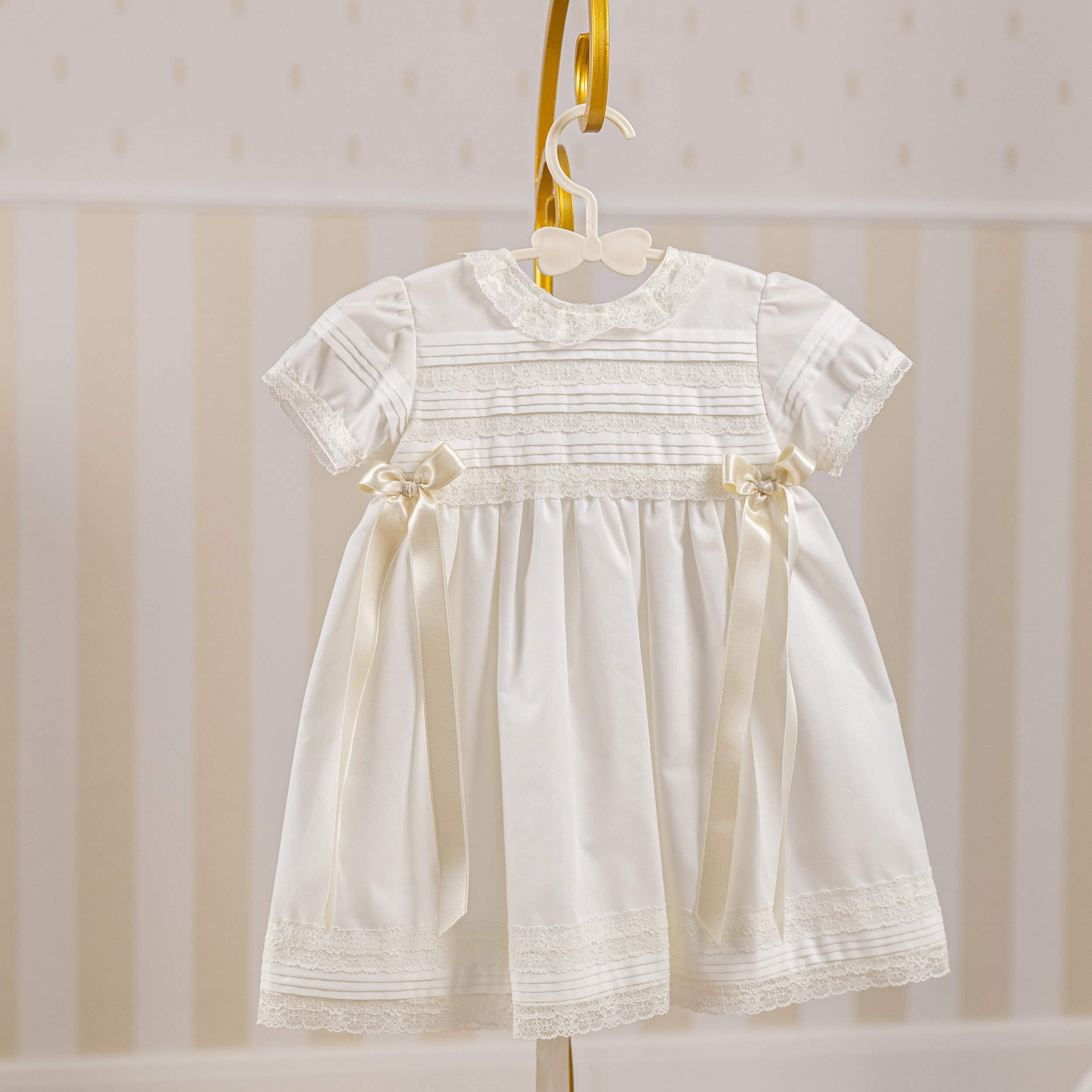 Cotton Christening Dress with lace details on a hanger against a striped background