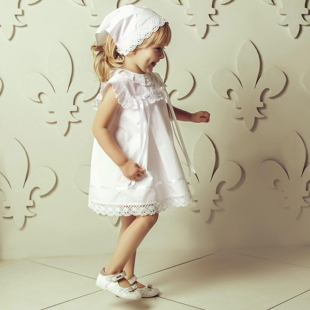 Young girl in aSummer Baptism Dress Set for Girl standing against a decorative wall.