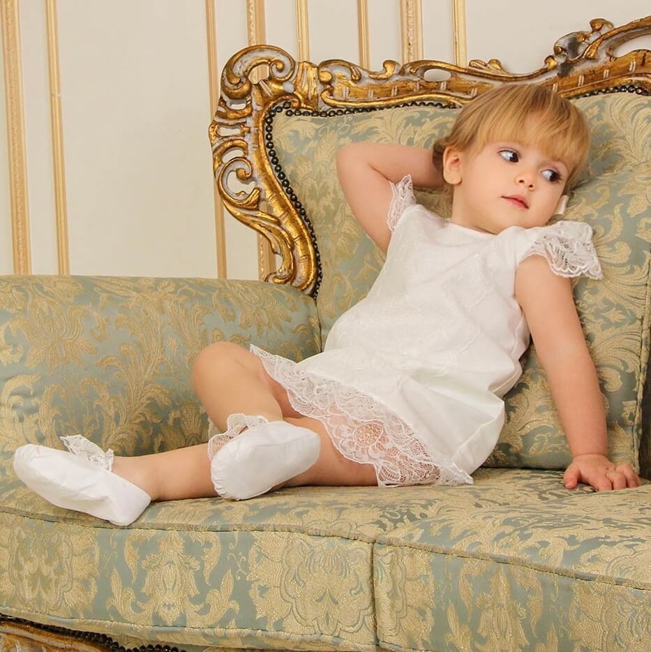 Young girl in a white dress sitting on an ornate couch.