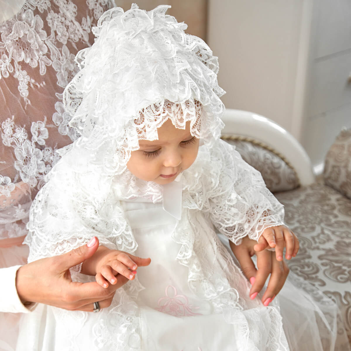 Child in a lace baptism bonnet sitting on a couch with a blurred background