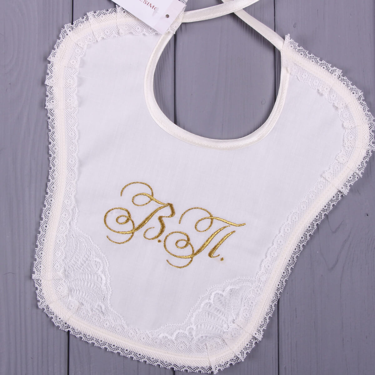 Newborn Lace Bib with gold lettering on a gray wooden surface