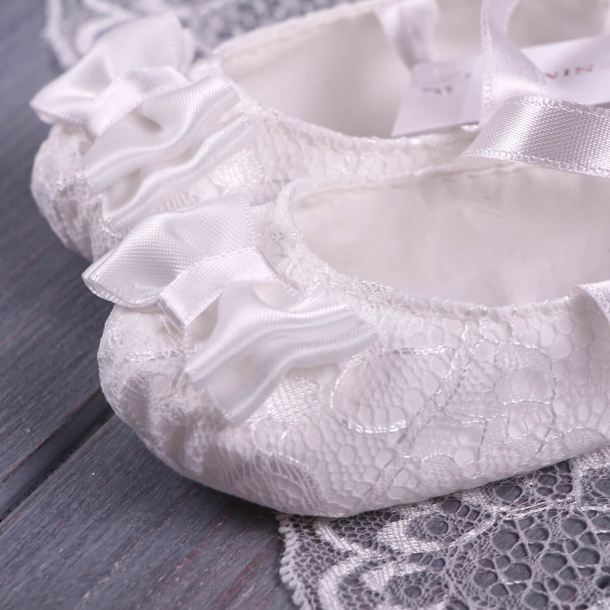 Christening Booties on a wooden surface with lace fabric underneath