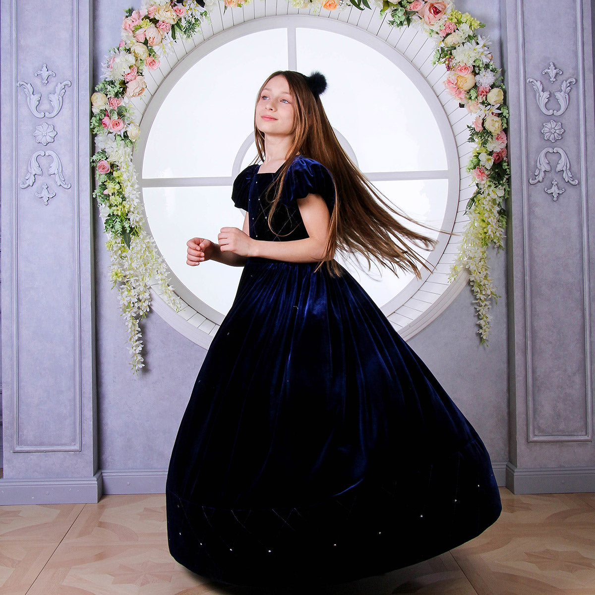 Woman in a dark blue dress standing in front of a decorative round window with floral decorations.