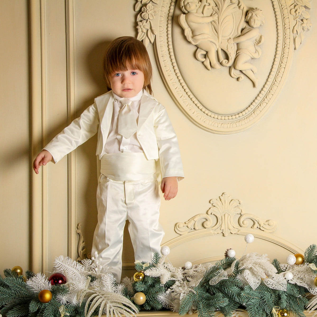Child in Baby Boy Baptism Suit standing in a decorated room with Christmas decorations.