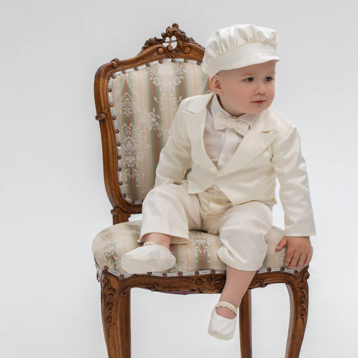 Baby in a Baby Boy Baptism Suit sitting on an ornate chair with a white background