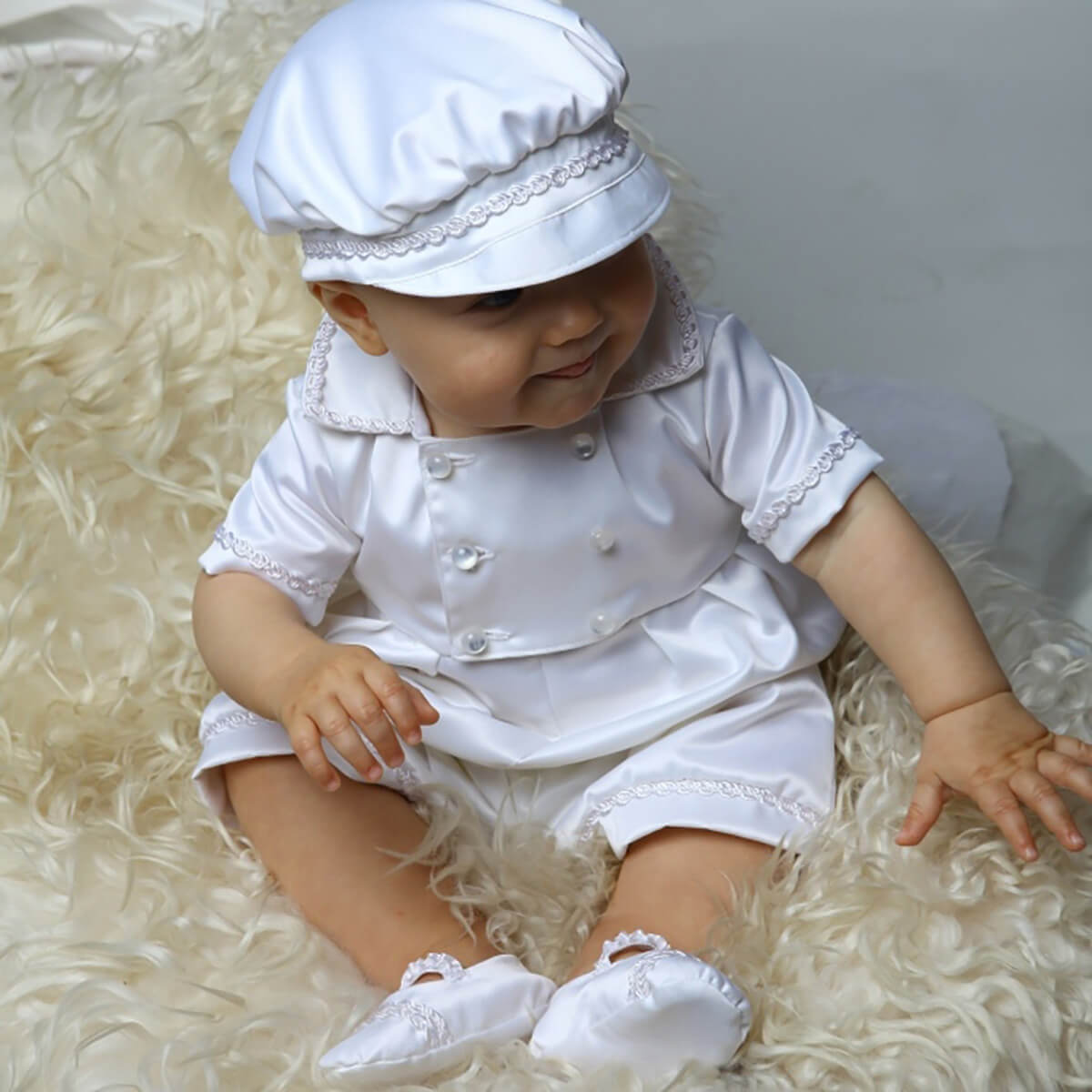 Baby in a Baby Boy Baptism Romper with a hat sitting on a textured surface