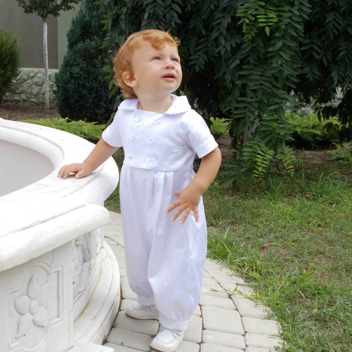 Child in a Baby Boy Baptism Romper standing on a stone path with greenery in the background