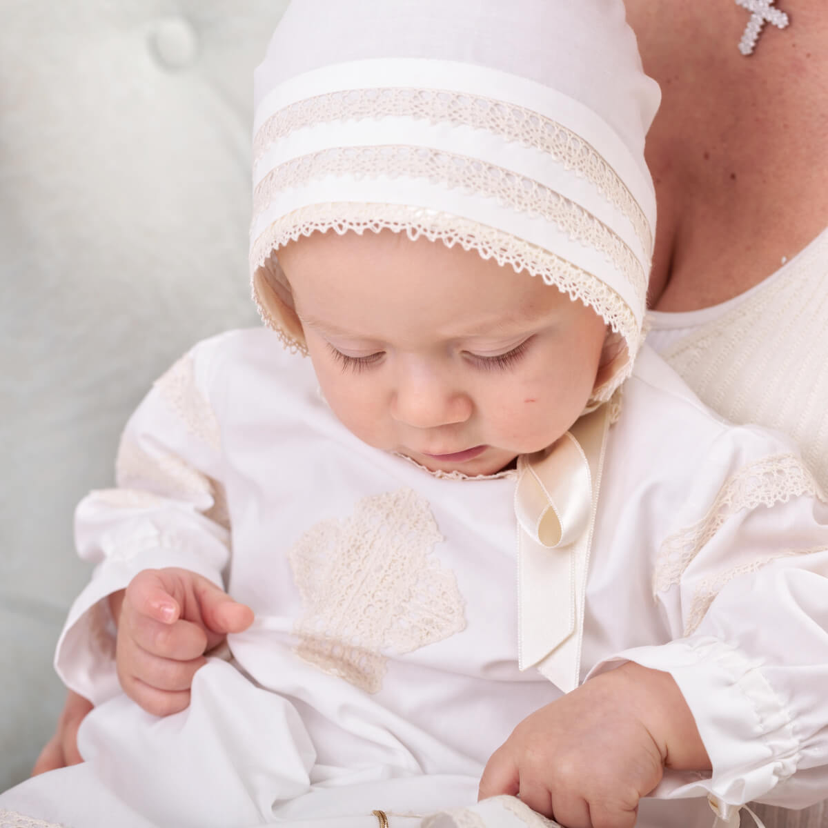 Baby in Baptism Gown with lace details, held by an adult against a neutral background