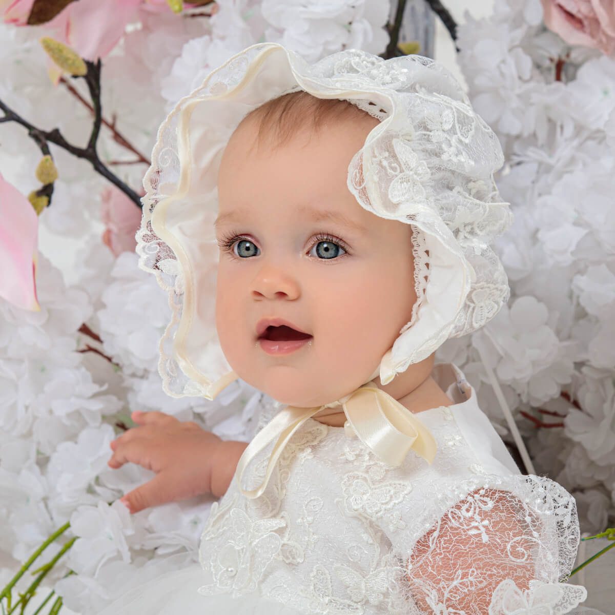 Baby in a vintage baby bonnet with a bonnet surrounded by white flowers and pink flowers.