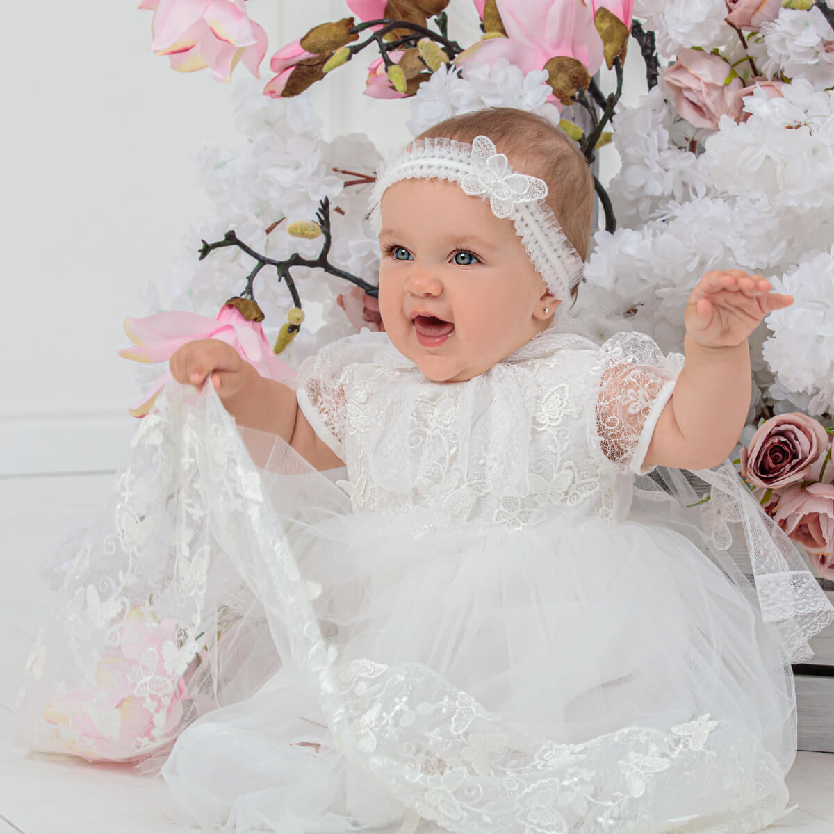 Baby in a Baptism Dress with Butterfly Lace surrounded by floral decorations
