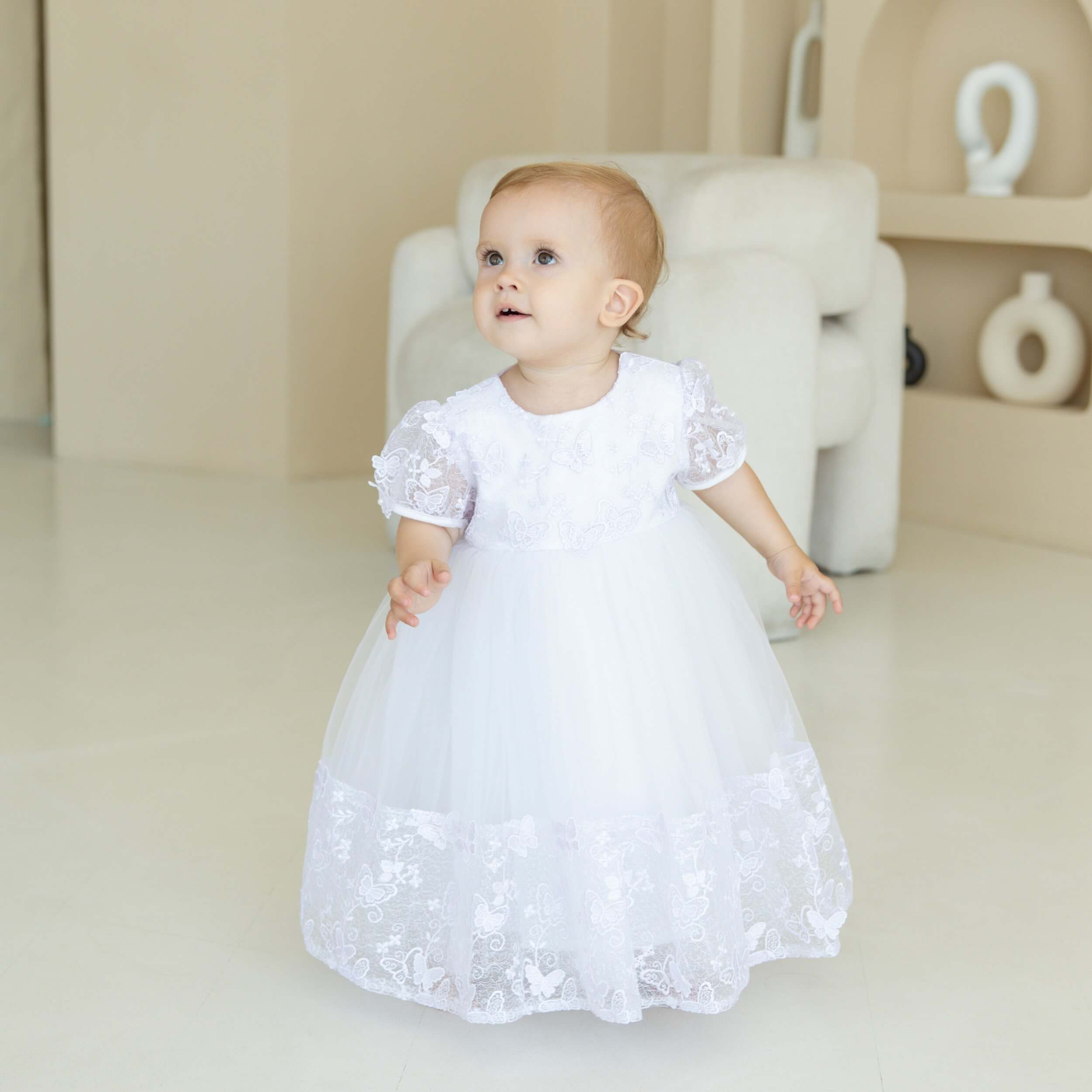 Baby in a Baptism Dress with Butterfly Lace standing in a softly lit room.