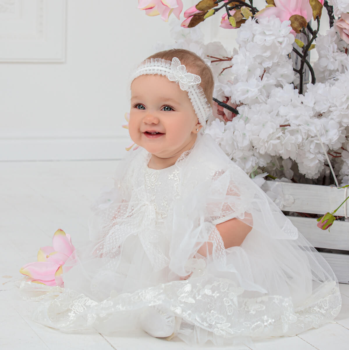 Girl in baby headband sitting on a white floor with floral decorations.