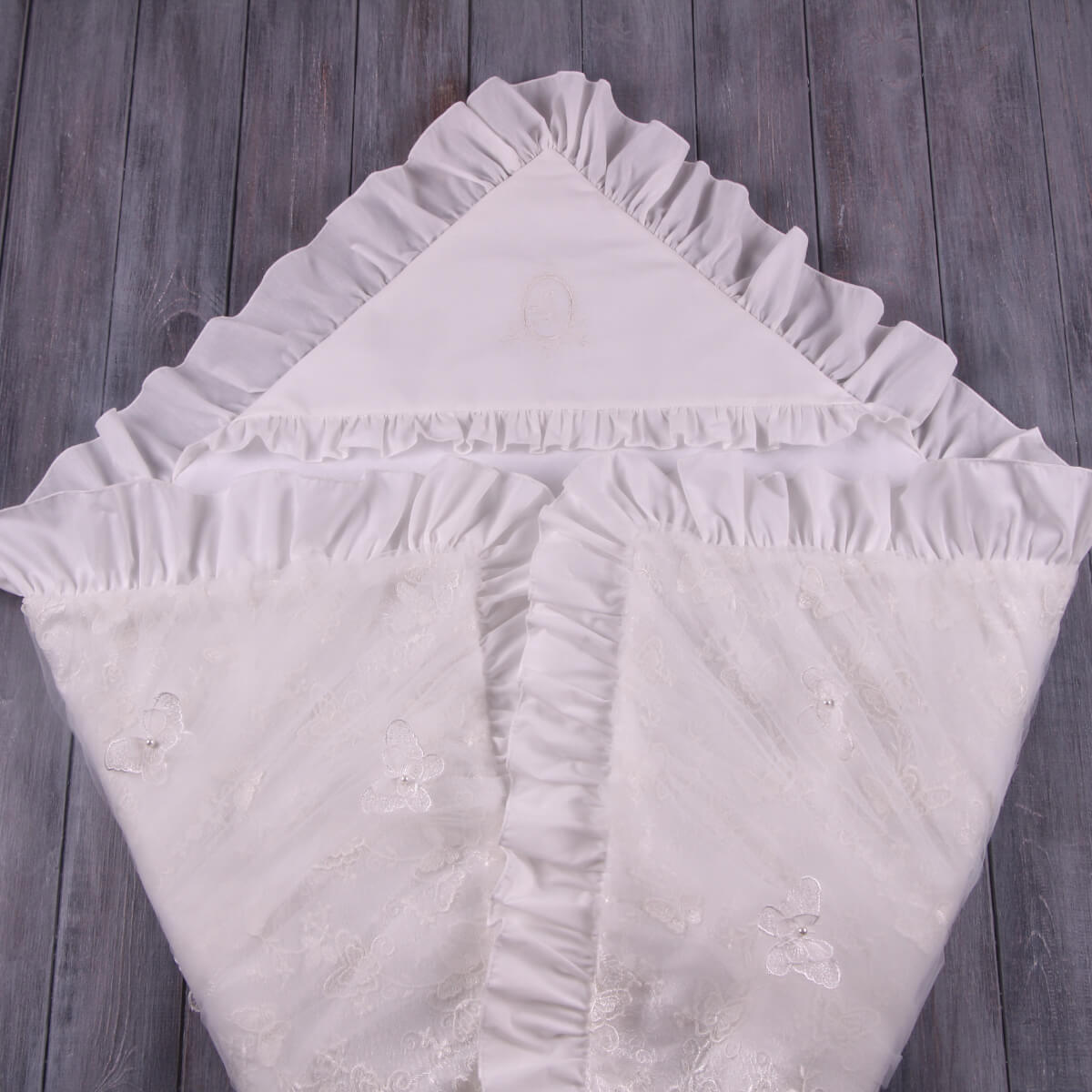 Stack of white ruffled christening blanket on a wooden surface