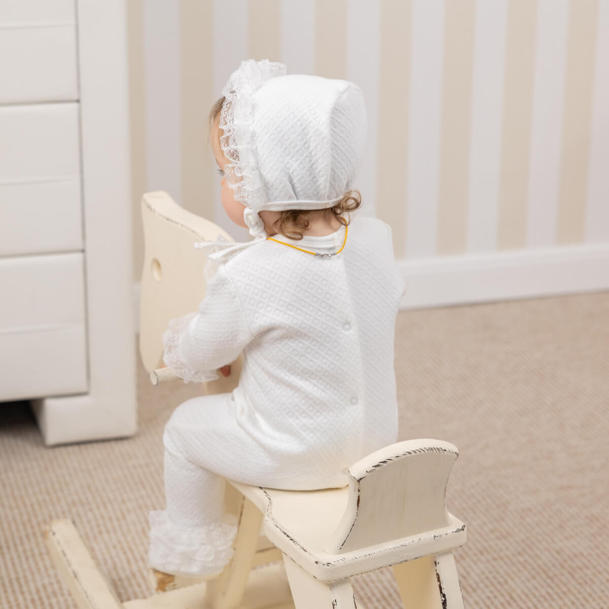 Child in a Coming Home Romper sitting on a chair in a room with white furniture.