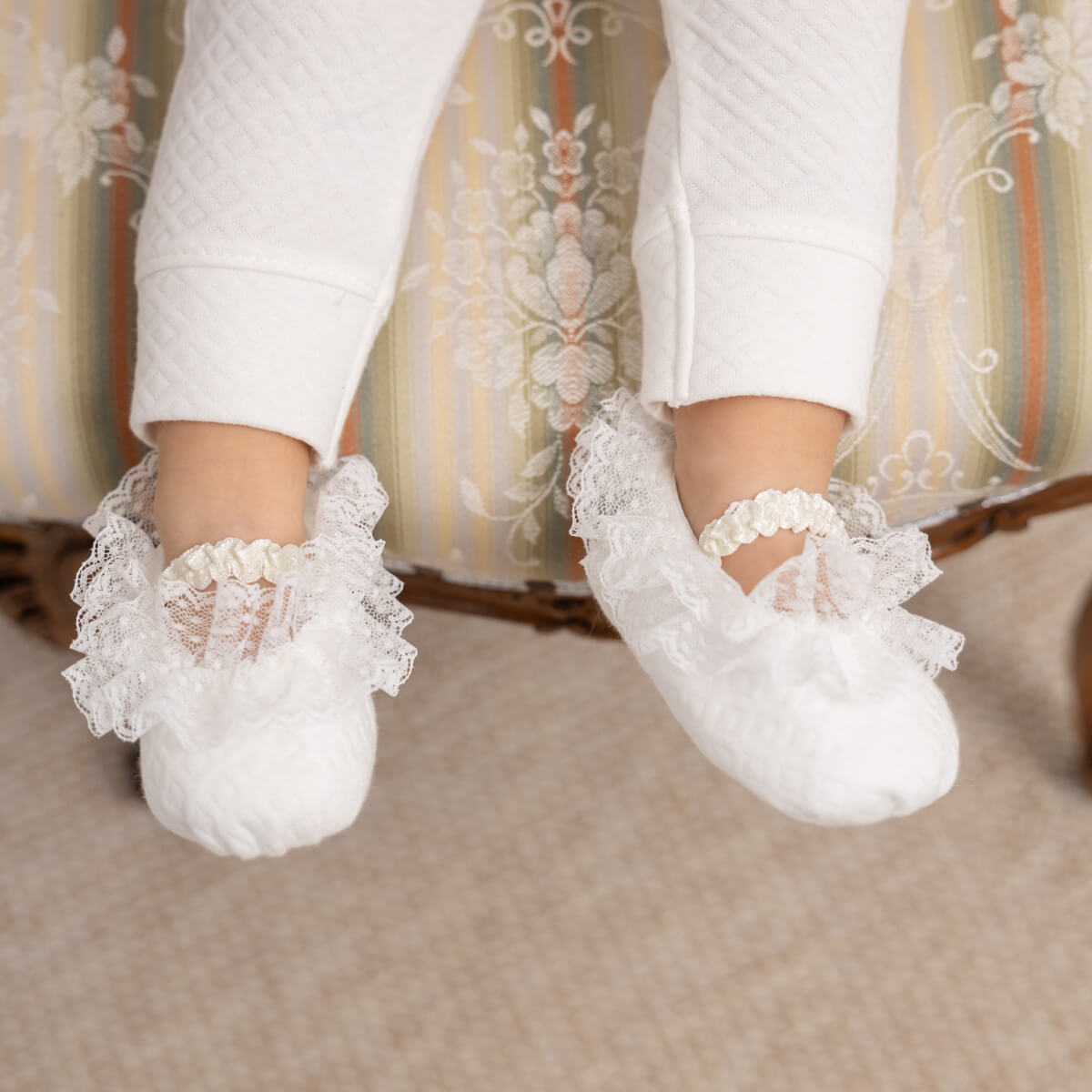 Christening Booties worn by a child with a patterned chair in the background