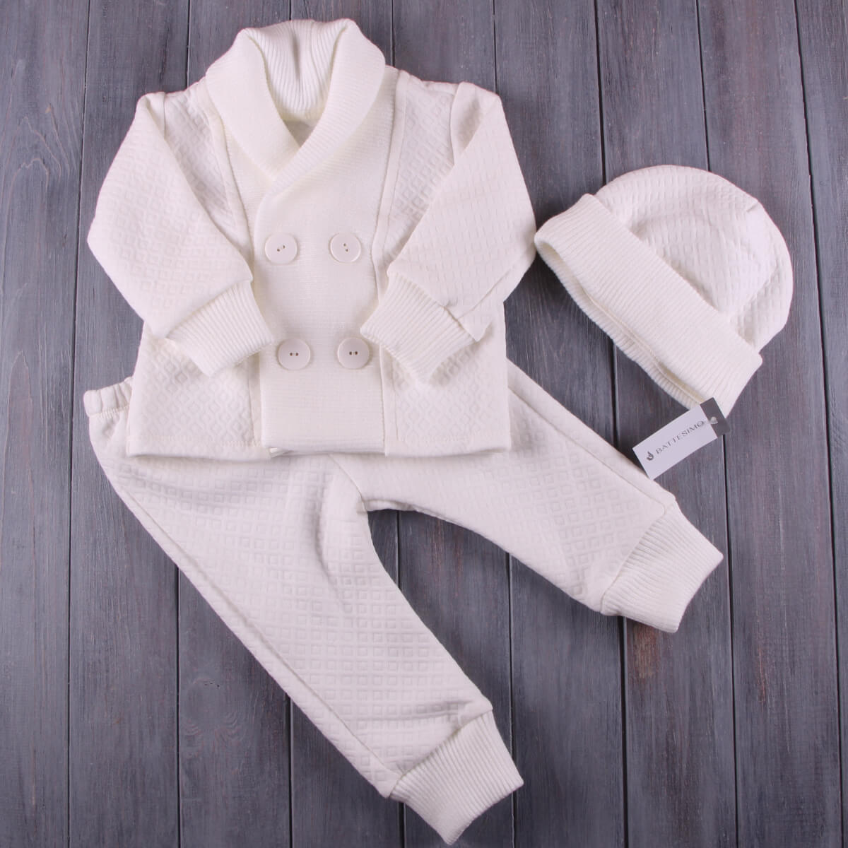White baby outfit with jacket, pants, and Boy Baptism Hat on a wooden surface