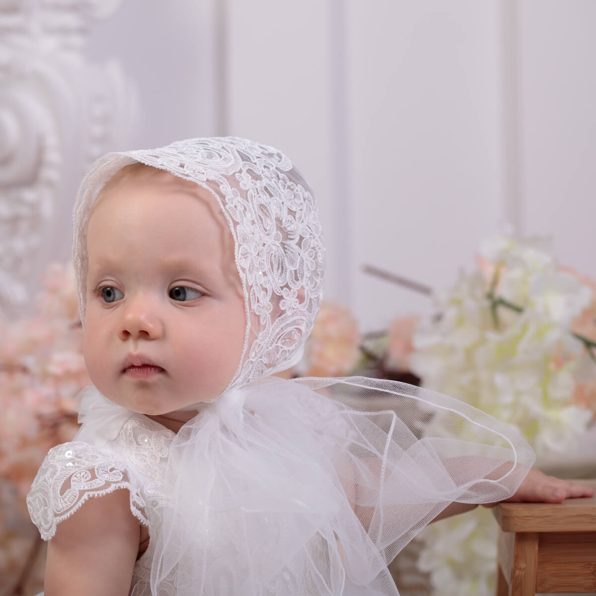 Baby wearing a Lace Baptism Bonnet in a softly blurred indoor setting