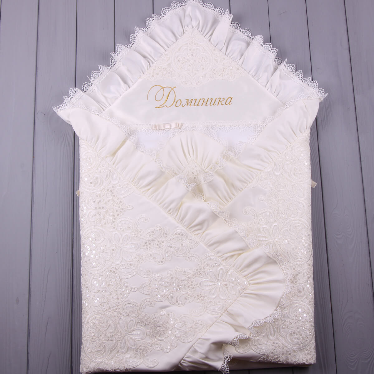 White embroidered christening blanket with lace details on a wooden surface