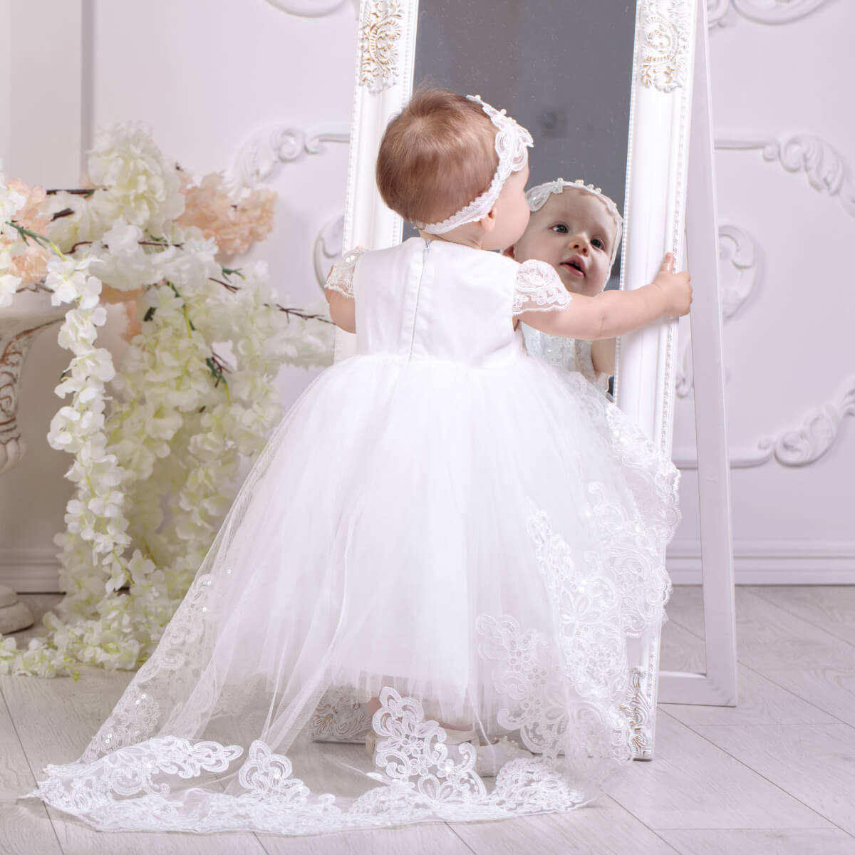 Baby in a Lace Baptism Dress with Train standing in front of a mirror.