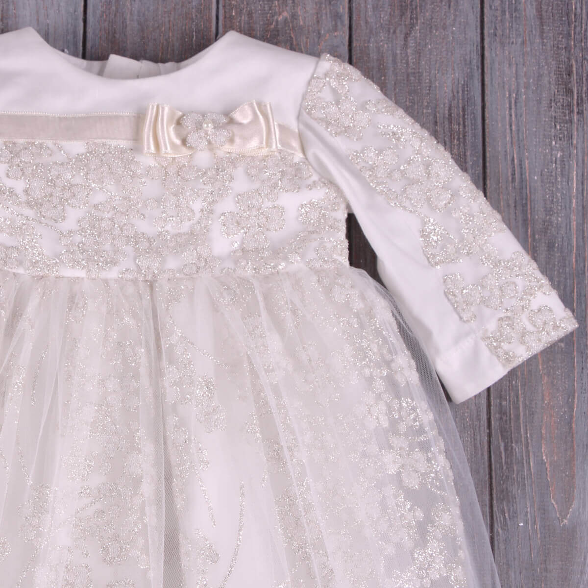 Christening Gown for Girls with decorative sleeves and bow on a wooden surface