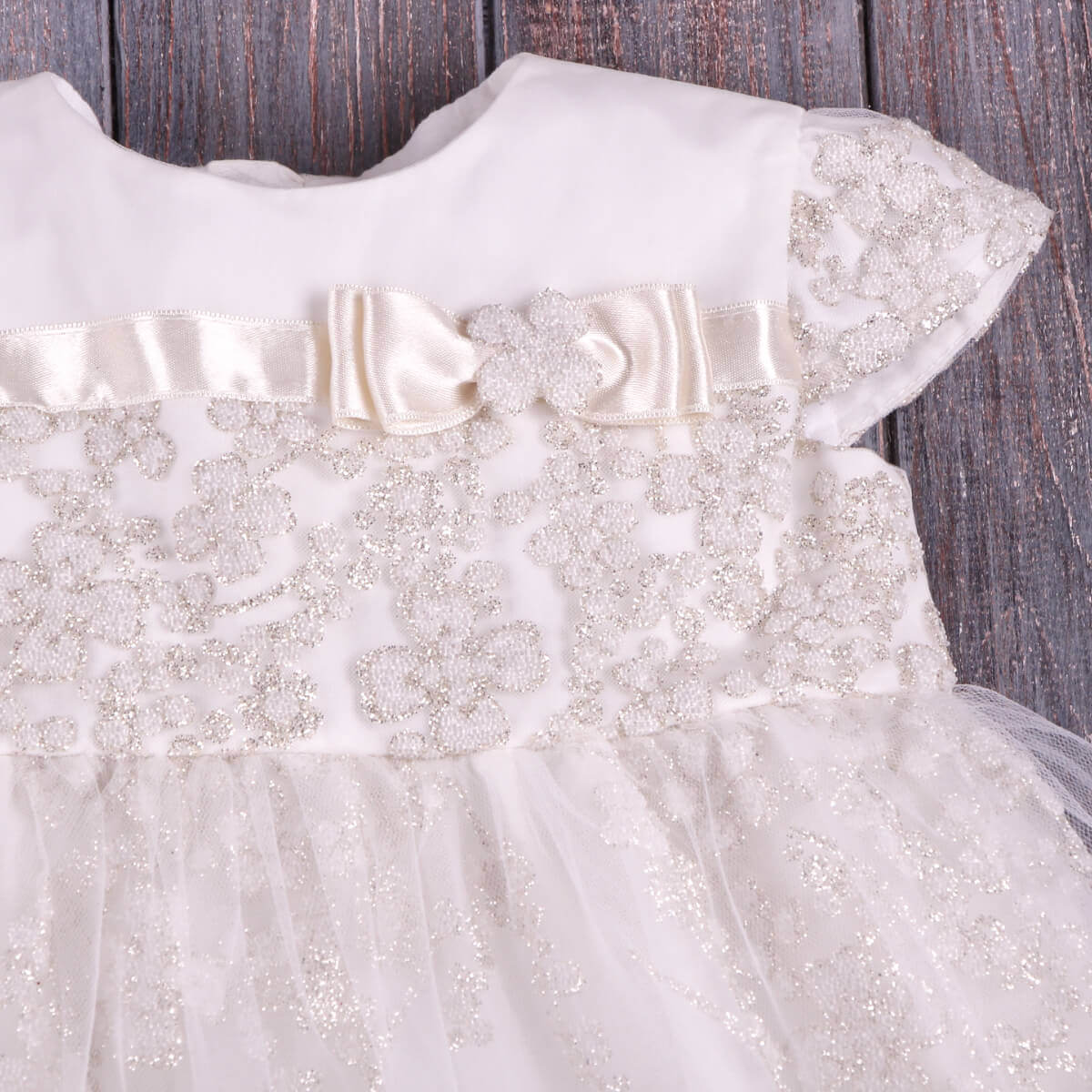 Baby Baptism Dress with decorative ribbons and embellishments on a wooden surface