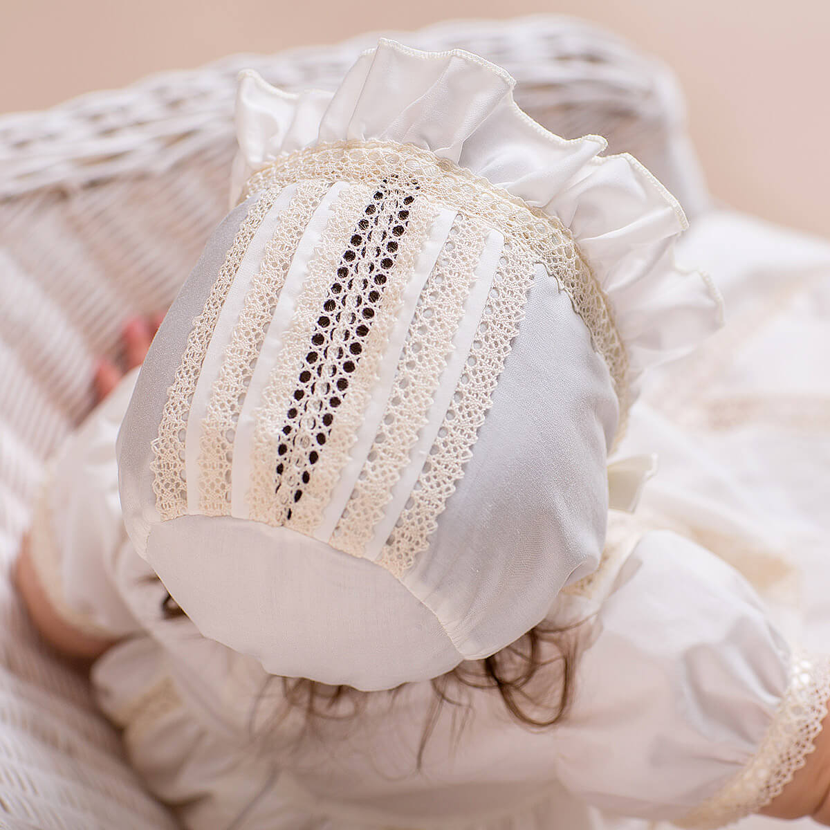 Close-up of aLace Baptism Bonnet with a baby wearing it, set against a soft pink background.