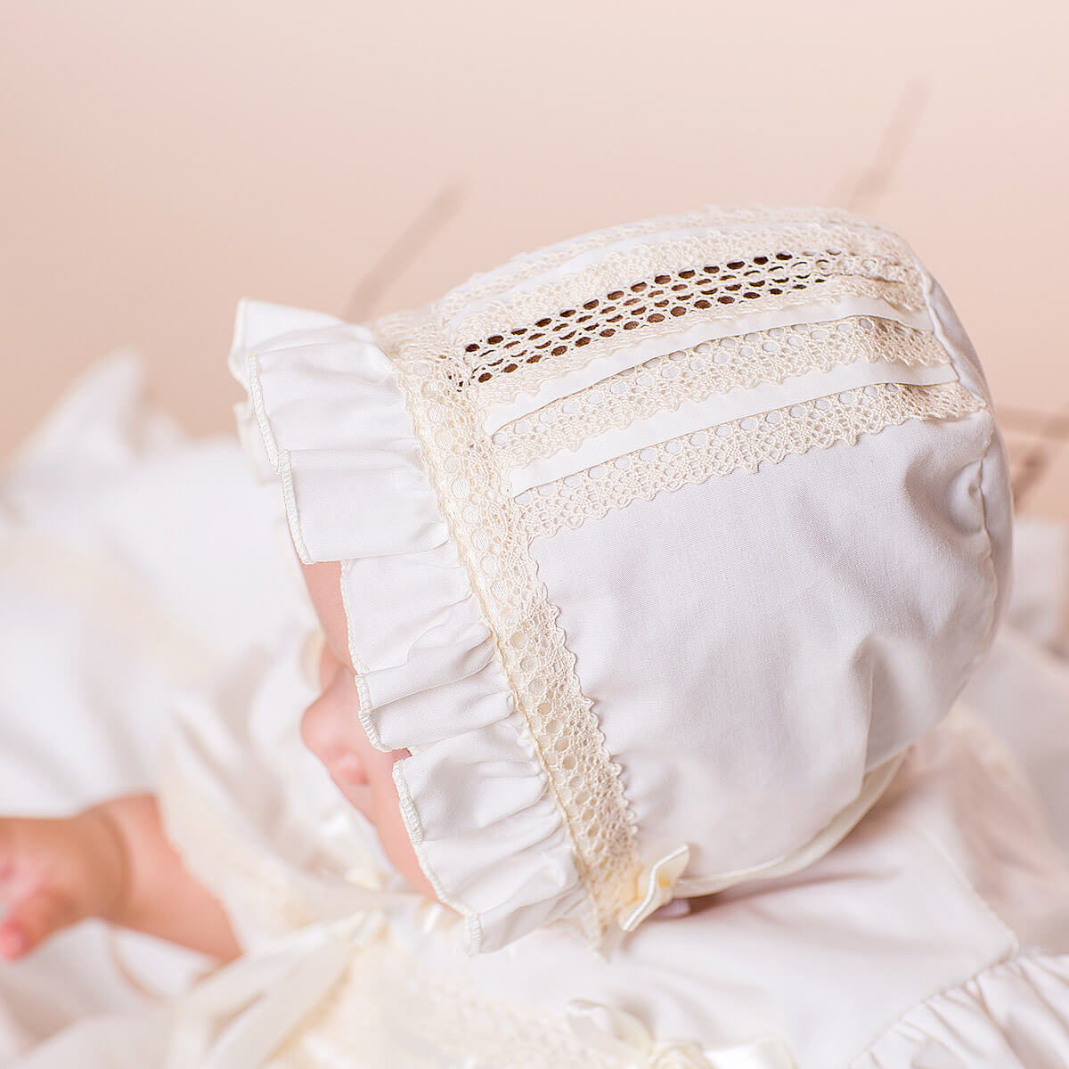 Close-up of a baby wearing a Lace Baptism Bonnet on a soft beige background.