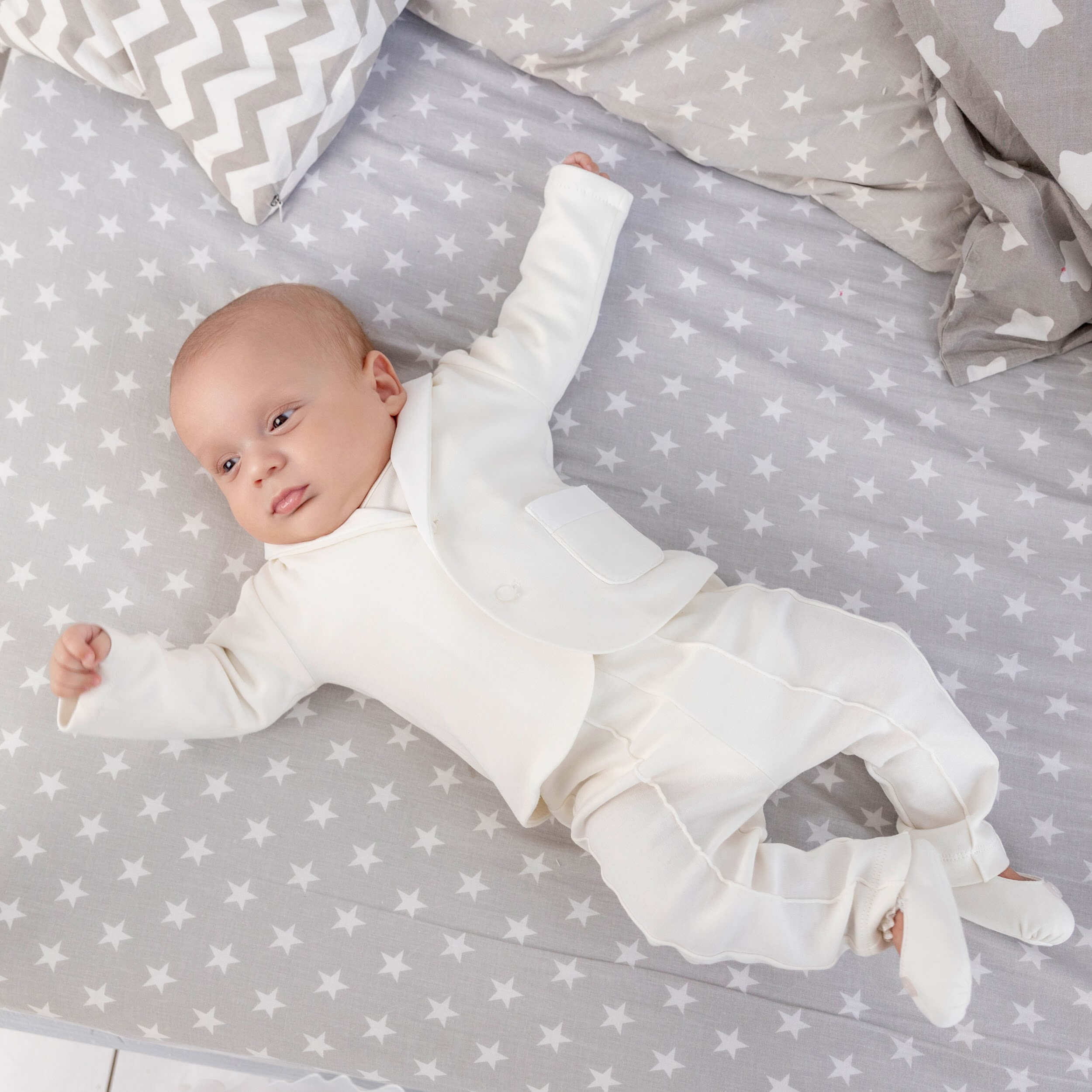 Baby in a Newborn Coming Home Suitl lying on a gray blanket with star patterns