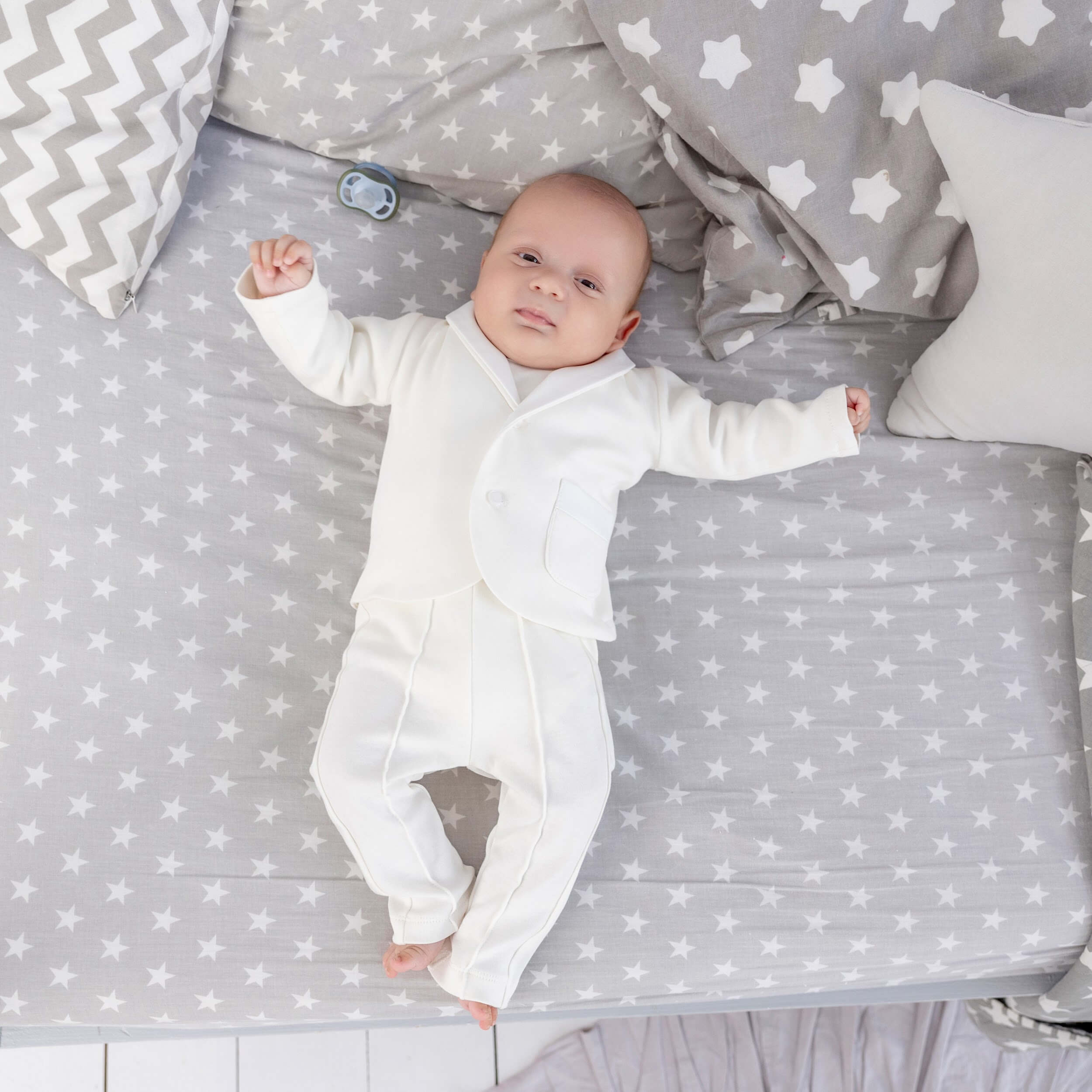 Baby in Newborn Coming Home Suit lying on a star-patterned blanket with gray and white checkered pillows.