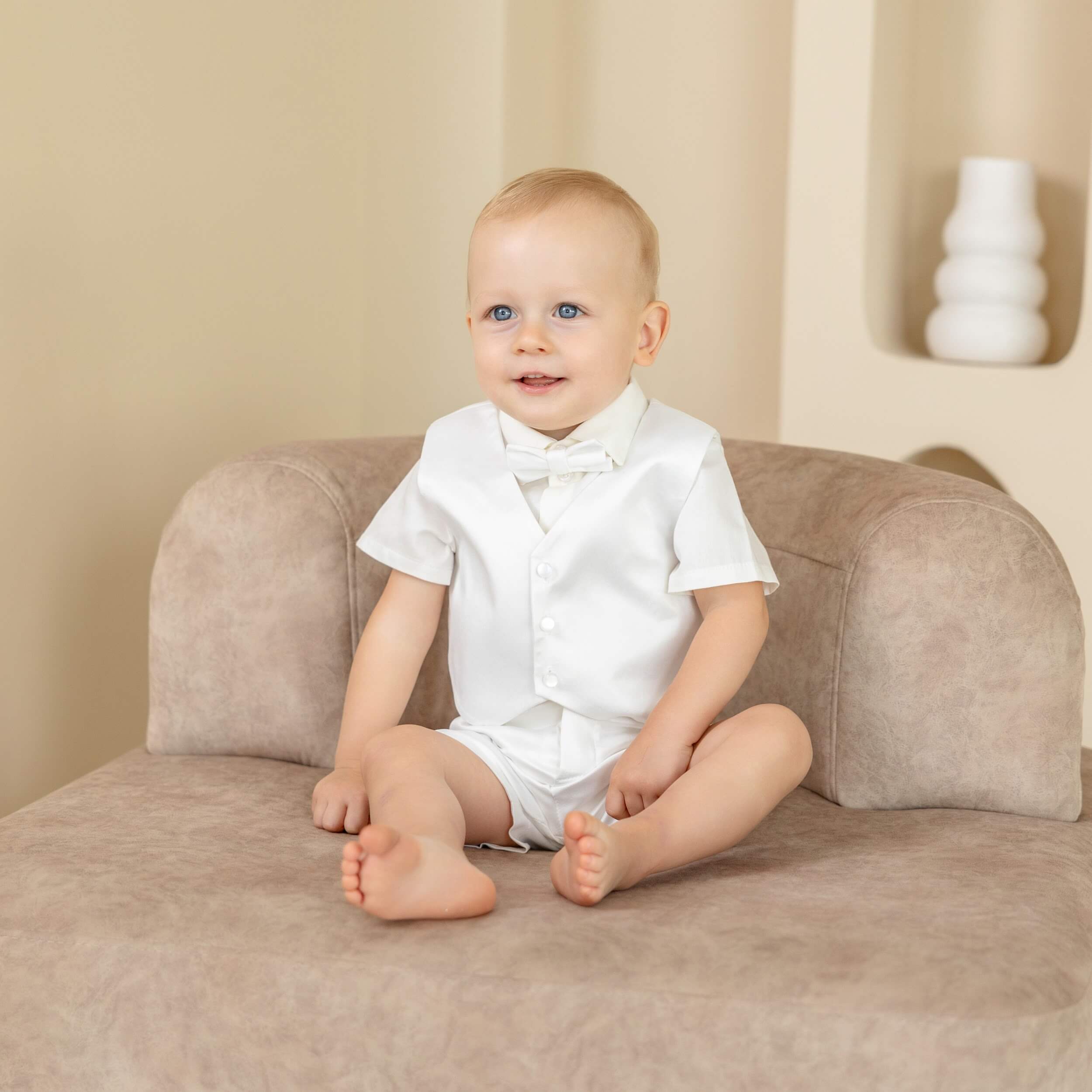 Baby sitting on a couch wearing a Baby Boy Christening Suit with a bow tie.