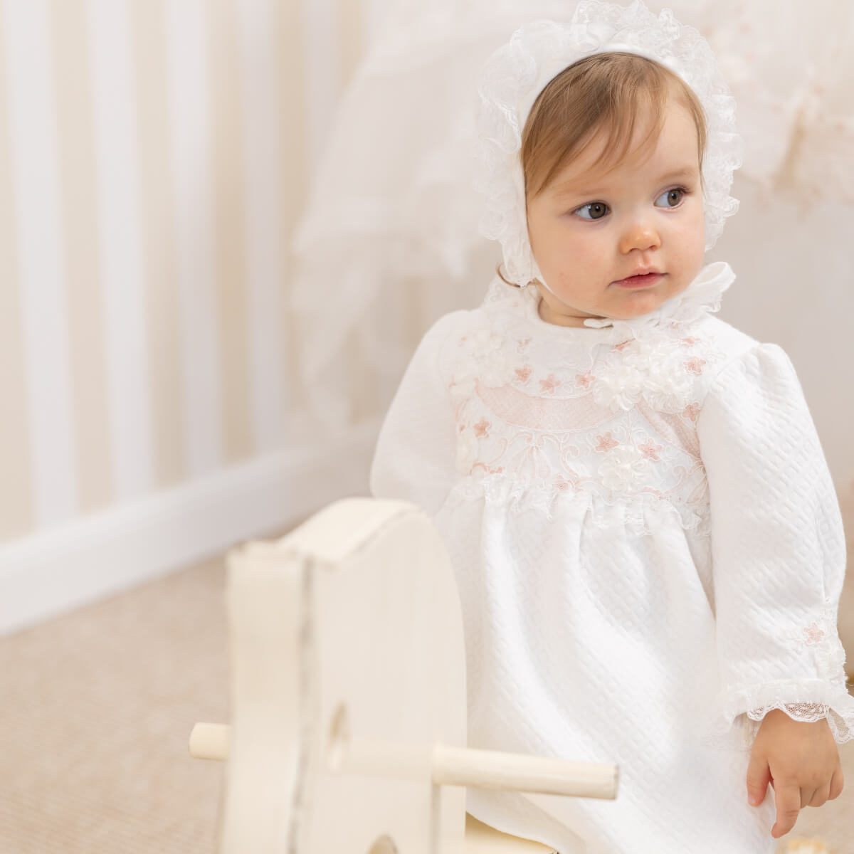 Baby in a Newborn Coming Home Dress sitting on a white chair.