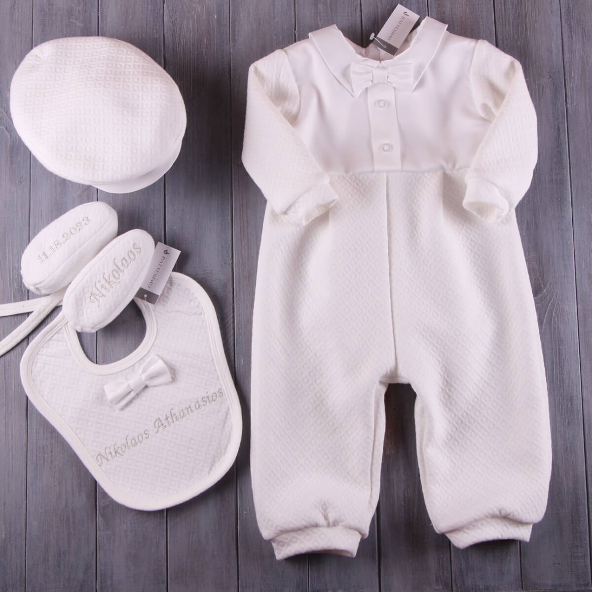 White baby outfit with hat, bib, and shoes on a wooden surface