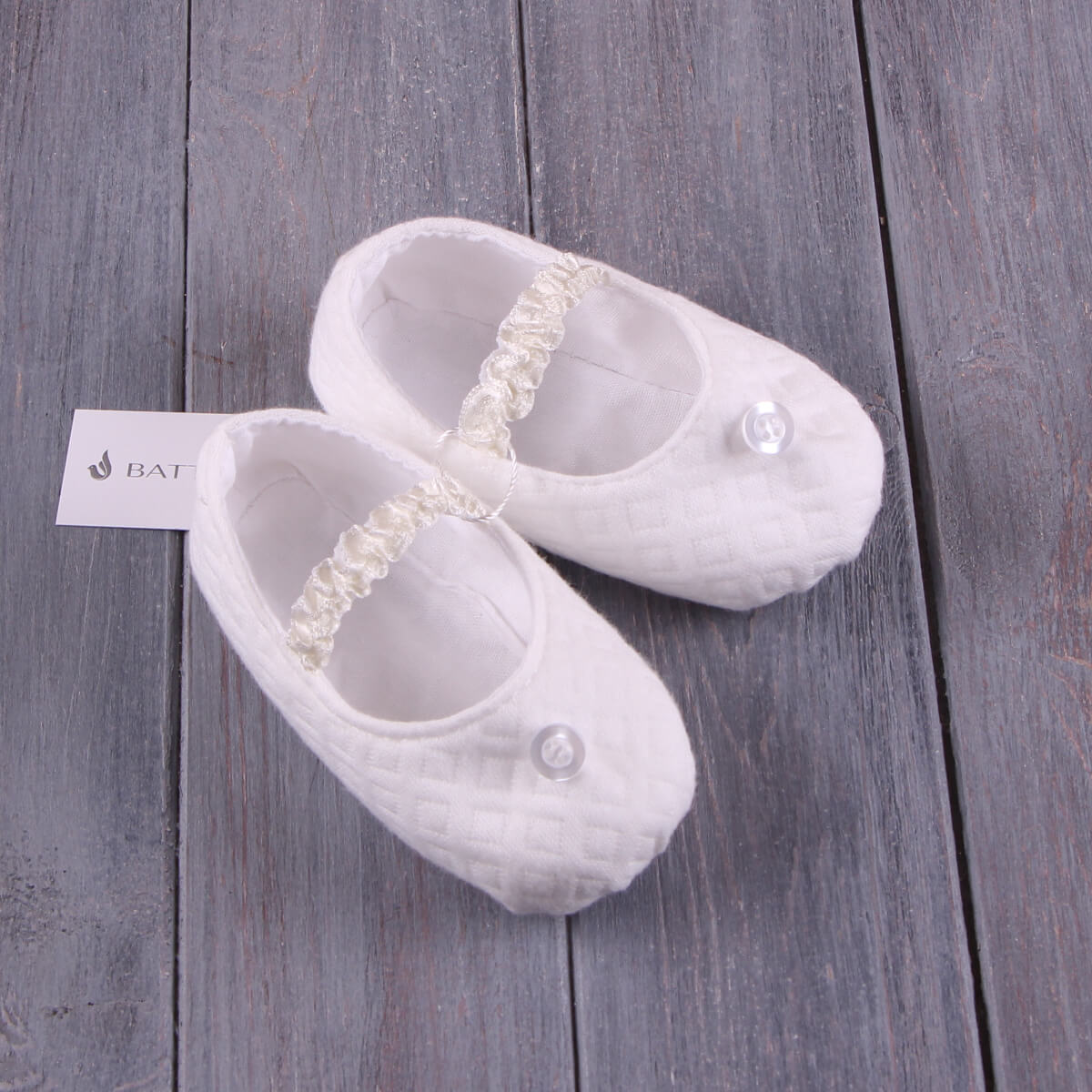 White baby shoes with decorative ribbons on a wooden surface