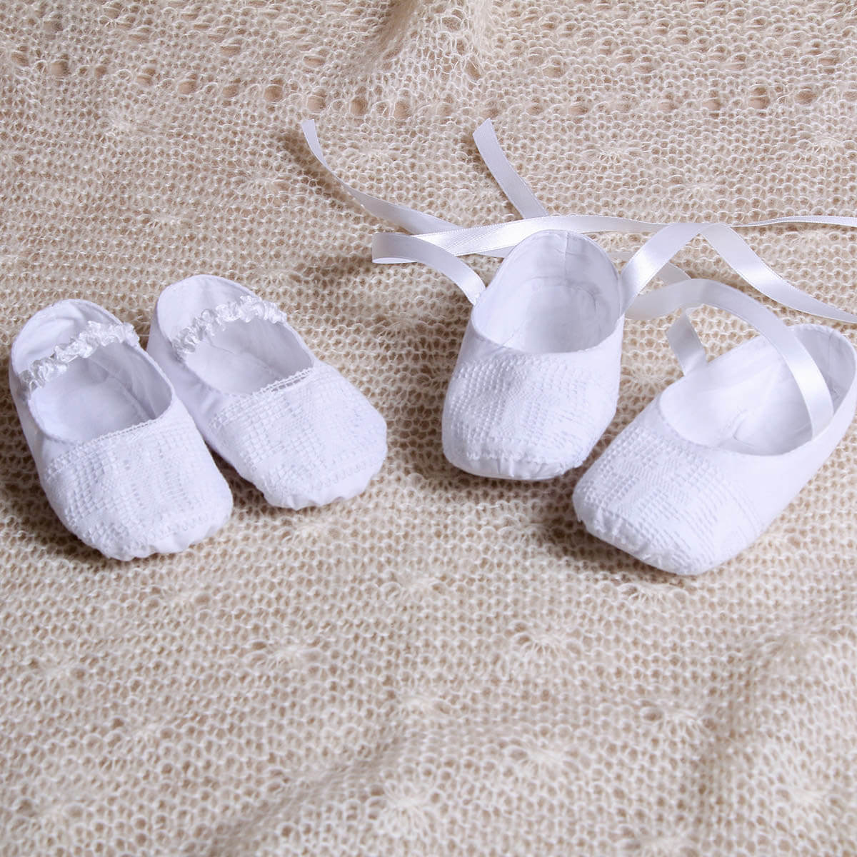Pair of Christening Booties on a textured beige fabric background