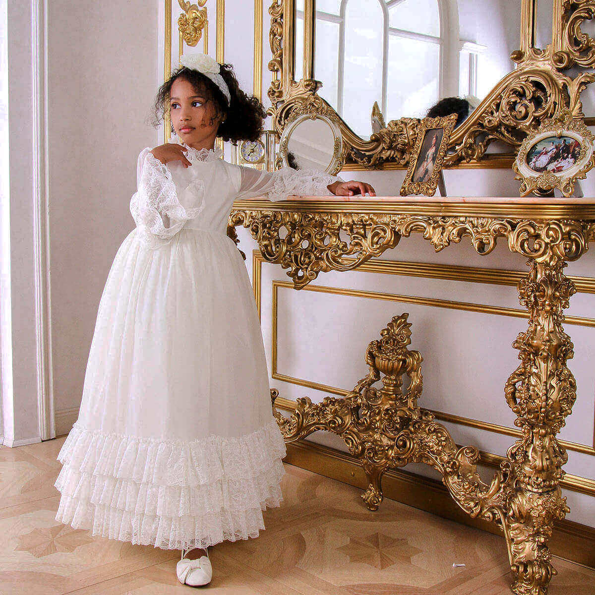 Young girl in Boho First Communion Dress standing next to an ornate gold mirror.