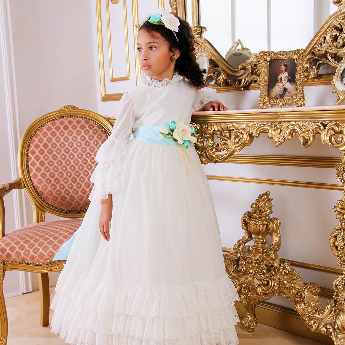 Young girl in Boho First Communion Dress standing in a room with ornate furniture.