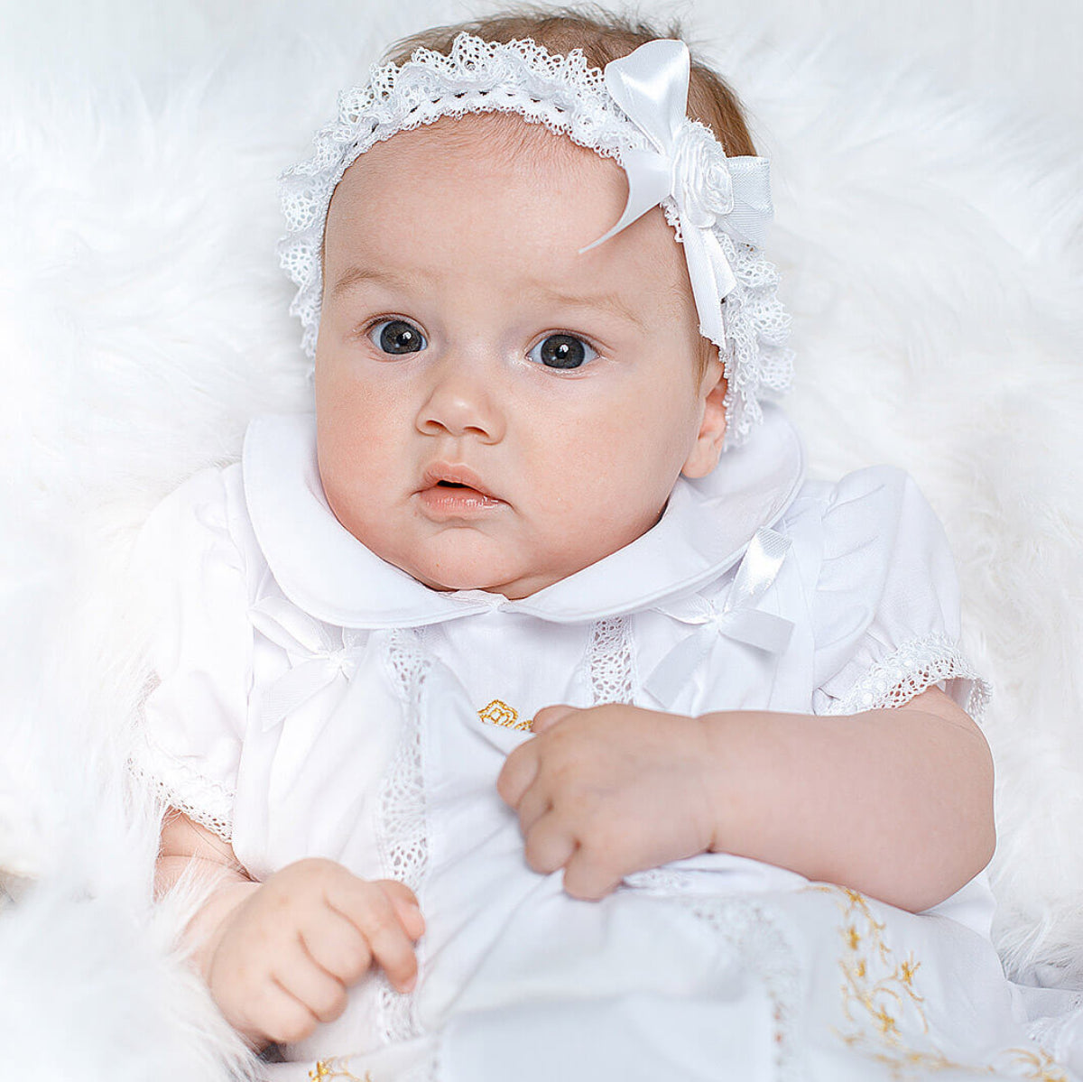 Baby in a white outfit with a lace headband on a white background